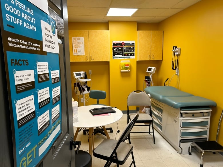 A look through the door to a medical room with bright yellow walls, a table and chairs, a table to lay on and other medical equipment.